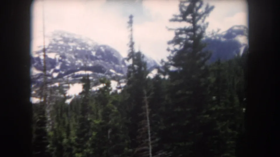 1962 8mm home-movie frame of tall pines and a rounded snow-patched mountain in Summit County, Colorado.