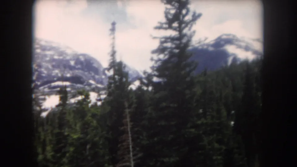 Final 8mm frame of a Summit County mountain landscape, with pine forest below snow-streaked slopes and visible home-movie softness.