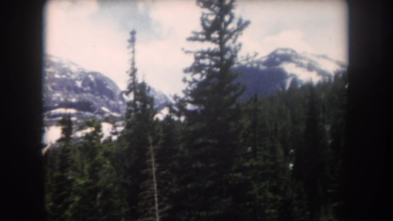1962 Summit County, Colorado 8mm frame showing dark film borders, conifer trees, and distant snowy mountain slopes.