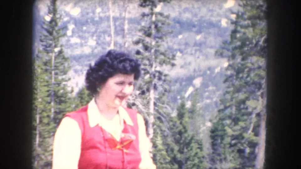 Adult woman in a red vest and white blouse stands smiling in a 1962 Summit County, Colorado mountain setting.