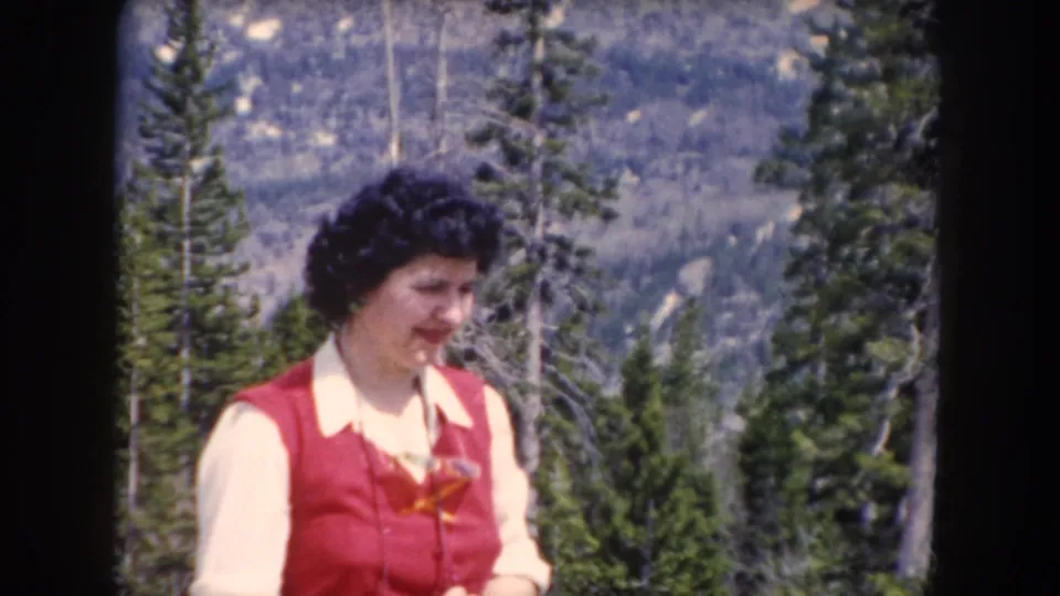 Adult woman in a red vest and light collared shirt in a Summit County, Colorado mountain forest, 1962 metadata supported.