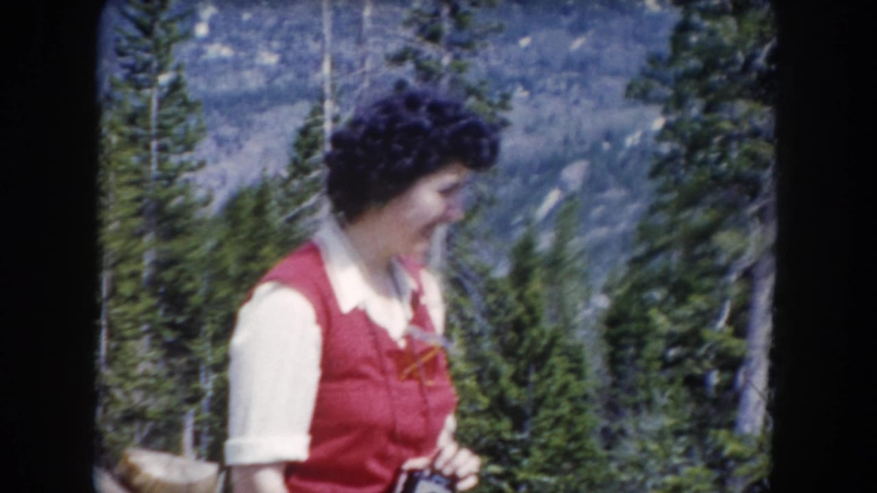 The woman turns slightly to the right in this 1962 Summit County mountain forest shot, with pine trees and a distant slope behind her.