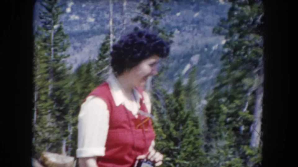 The woman turns slightly to the right in this 1962 Summit County mountain forest shot, with pine trees and a distant slope behind her.