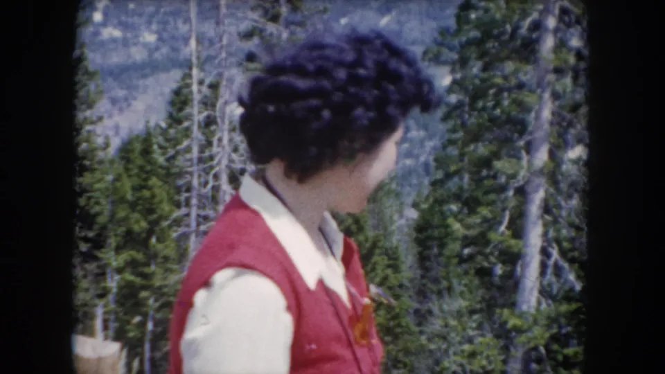 The woman turns in profile in the Summit County mountain forest, with conifers and a distant slope behind her.