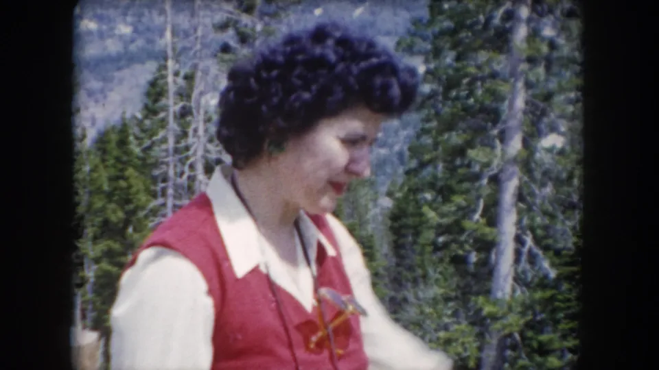 The woman appears in profile in 1962 Summit County, Colorado home-movie footage, standing before trees and rocky mountain terrain.