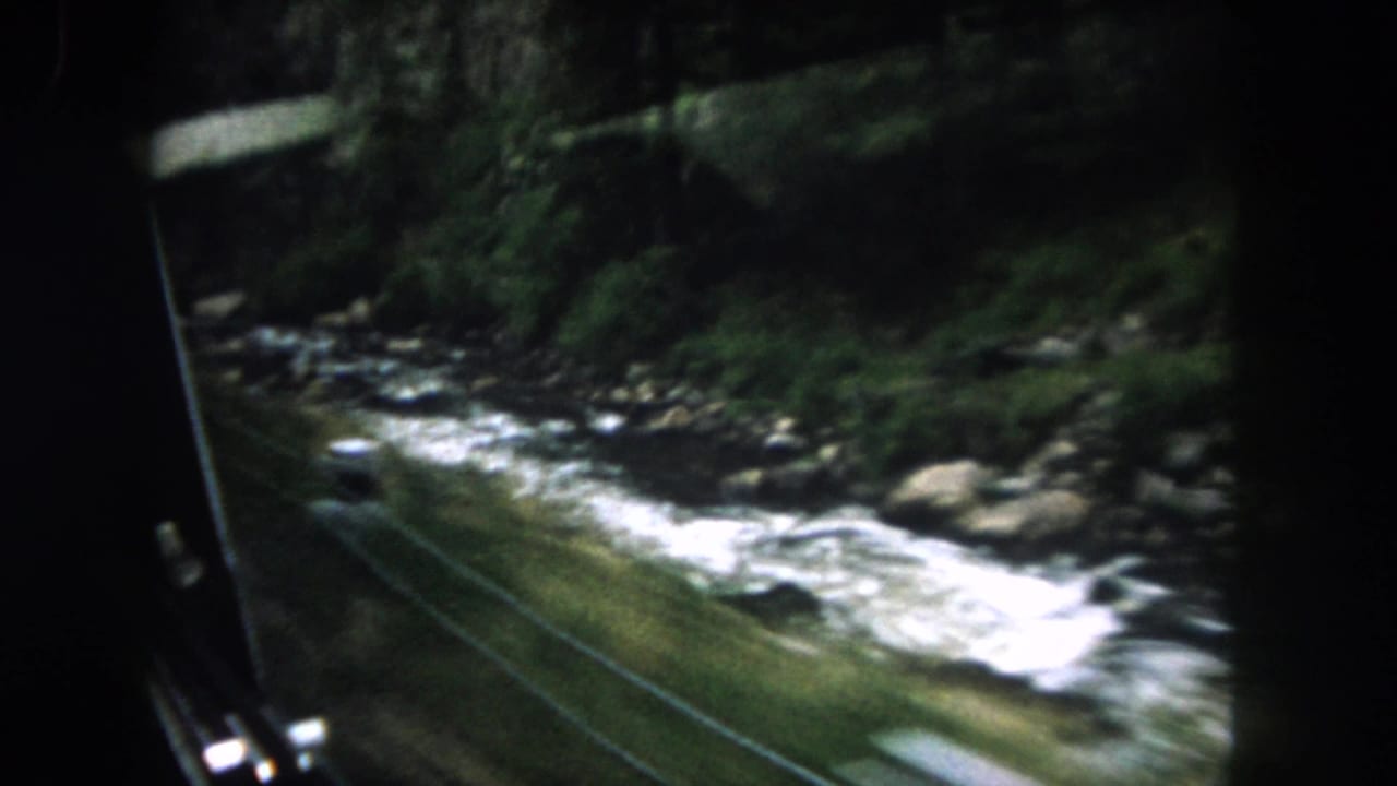 1962 Summit County, Colorado travel footage shows a rushing river beside trees and rocks, framed partly by the moving vehicle window.