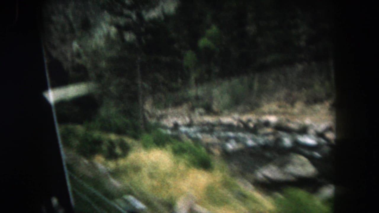 1962 Summit County, Colorado view of a rocky stream, grass, and trees filmed from a moving vehicle.