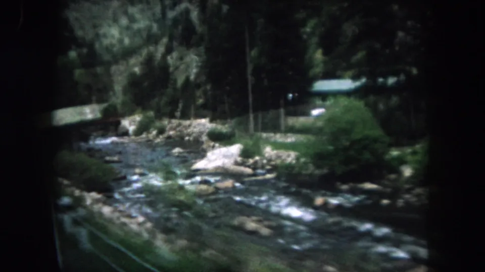 A blurred 1962 Summit County roadside view shows whitewater, rocks, trees, and a low bridge or rail along the river.