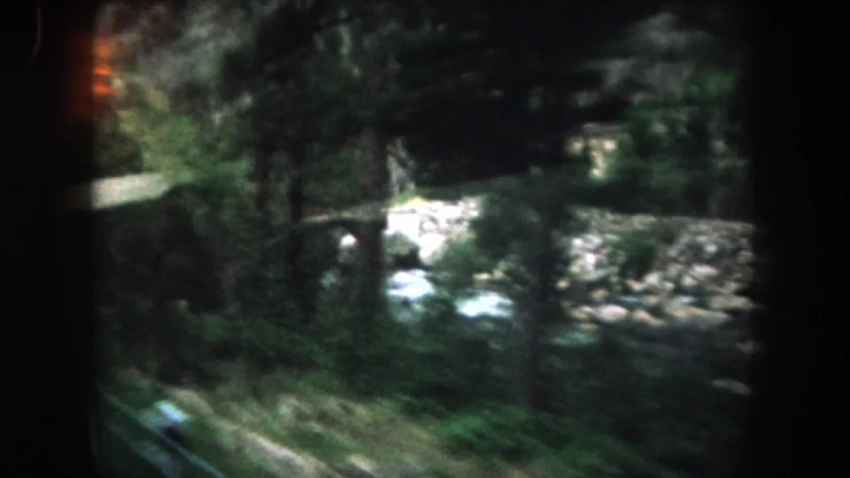 A soft 1962 Summit County car-window frame shows river rocks, whitewater, green banks, and trees passing close to the lens.
