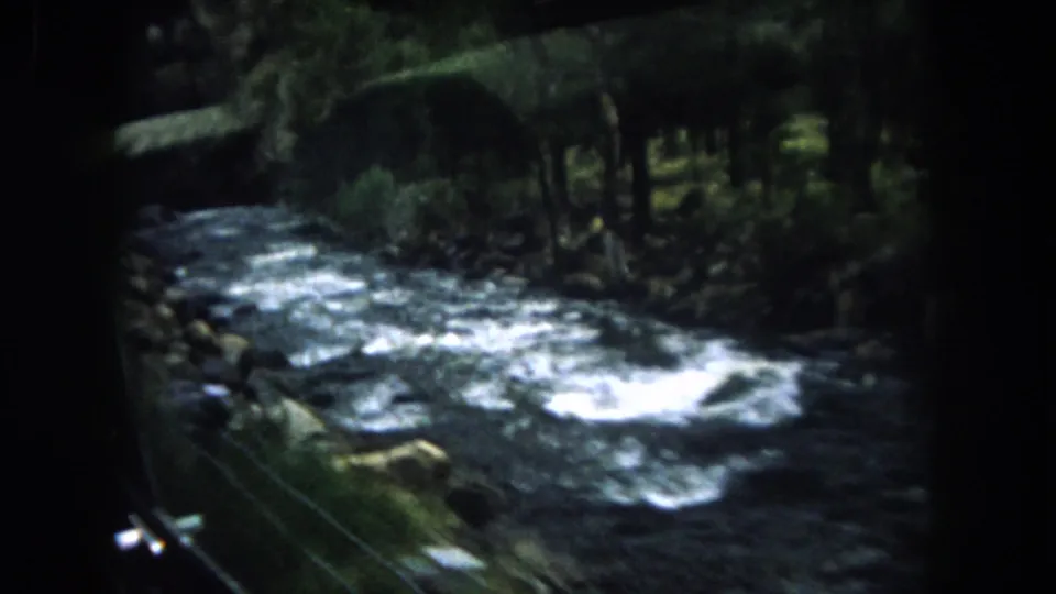 1962 Colorado 8mm frame of a swift river with whitecaps, rocks, and wooded banks filmed from transit.