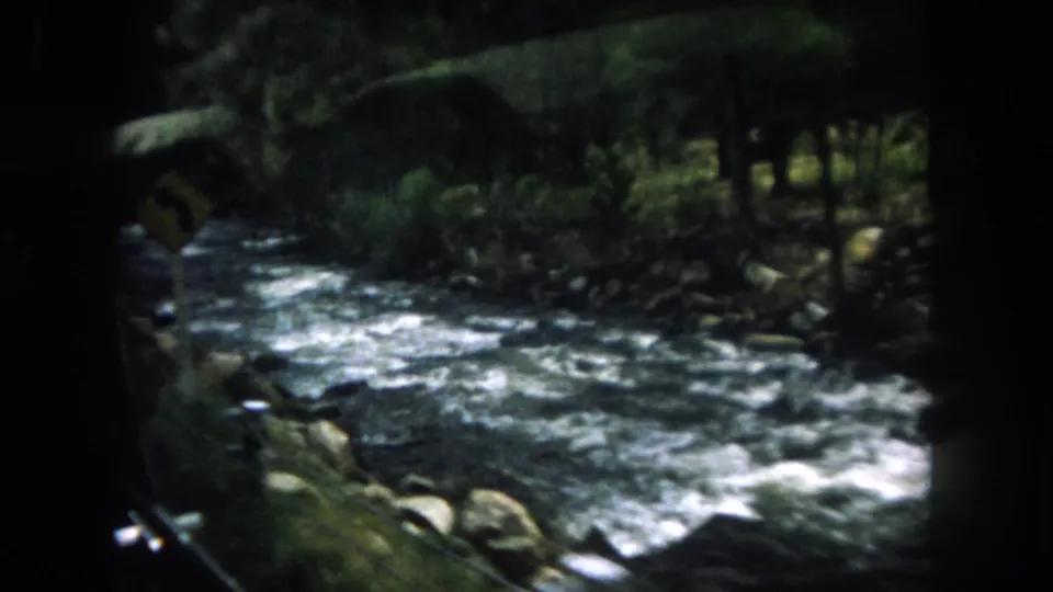 1962 Summit County, Colorado river rapids framed by dark vehicle edges, with rocky banks and forest visible beyond.