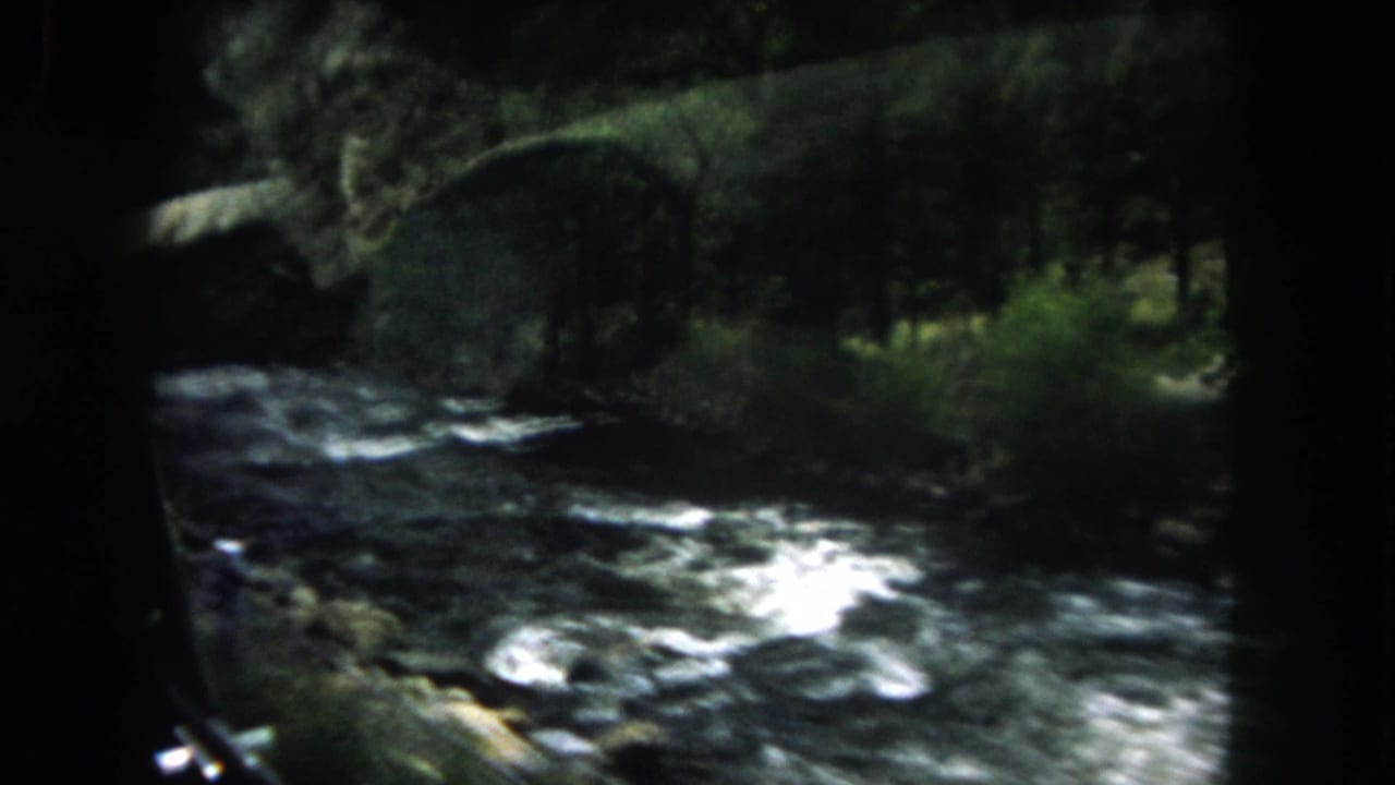 Passenger view of a white-water river running beside a wooded Summit County road in 1962 home-movie footage.