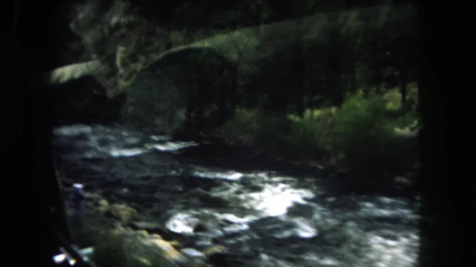 Passenger view of a white-water river running beside a wooded Summit County road in 1962 home-movie footage.