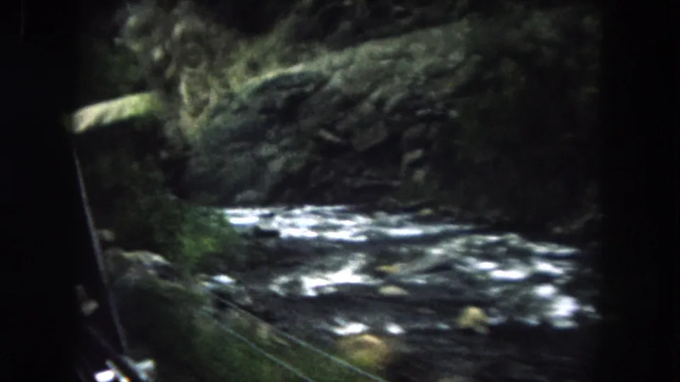 Summit County 8mm road footage showing a rushing river, rocks, and green wooded banks from inside a passing car.