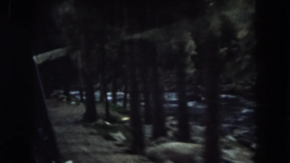 End frame from the 1962 Summit County drive, with tree trunks, boulders, and a stream visible in dark moving 8mm footage.