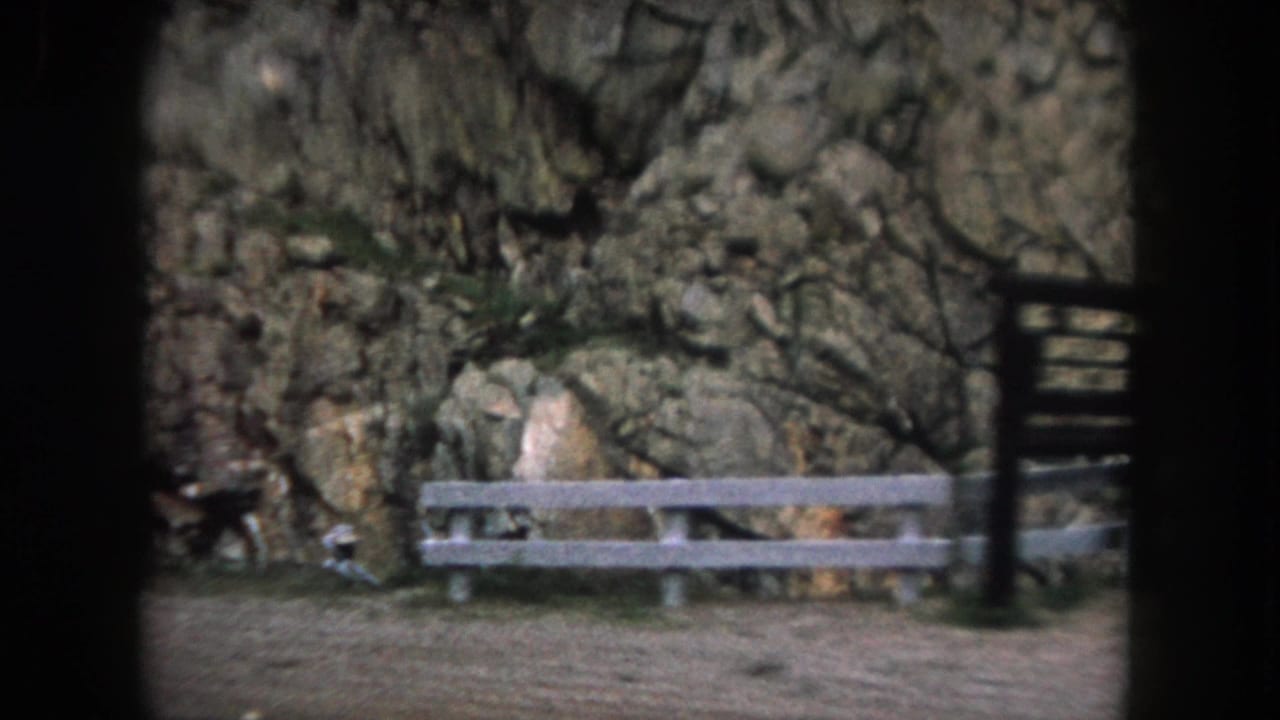 White roadside fence and dark signpost in front of a rocky cliff.