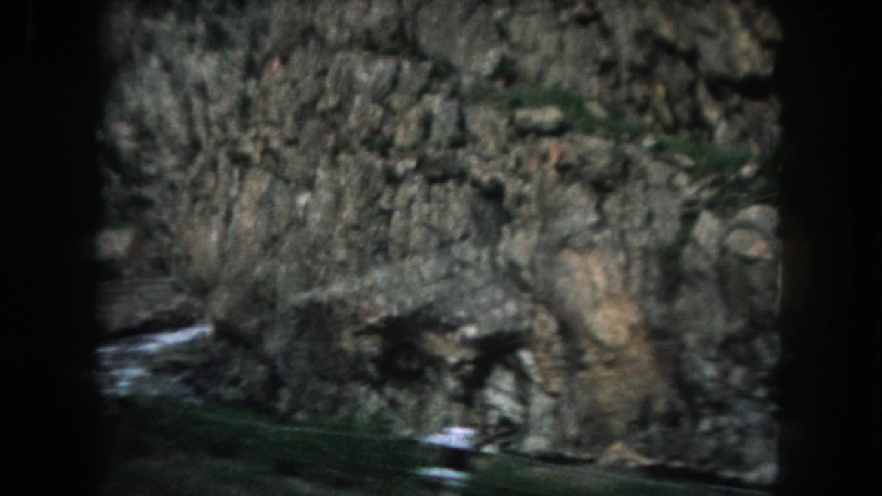 Rock face with brush and a narrow stream at the base.