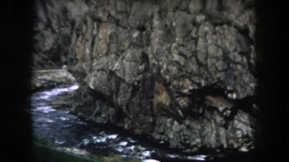 1962 8mm home-movie view of water moving along the base of a rocky Summit County roadside cliff.