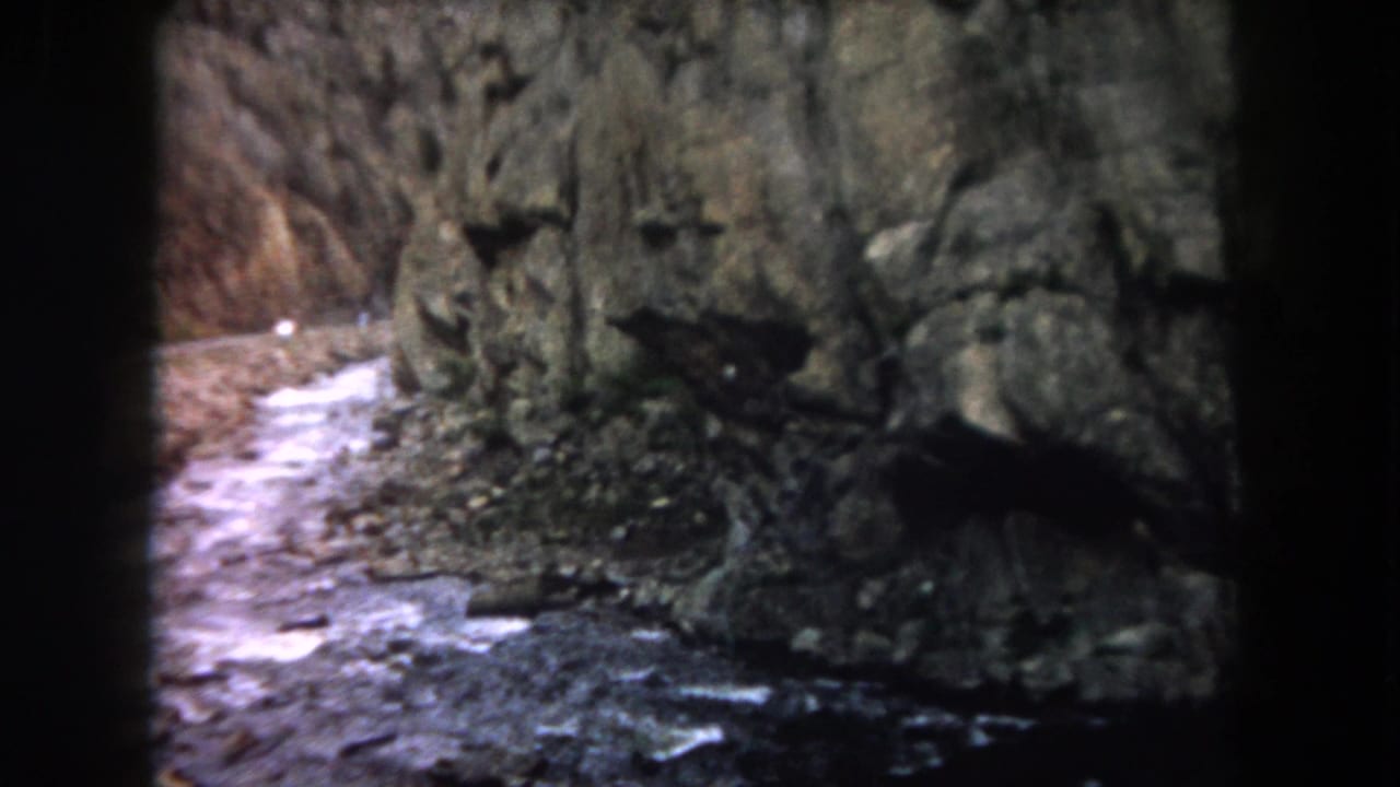 Rushing river beside steep canyon rock walls seen through dark vehicle-window edges.