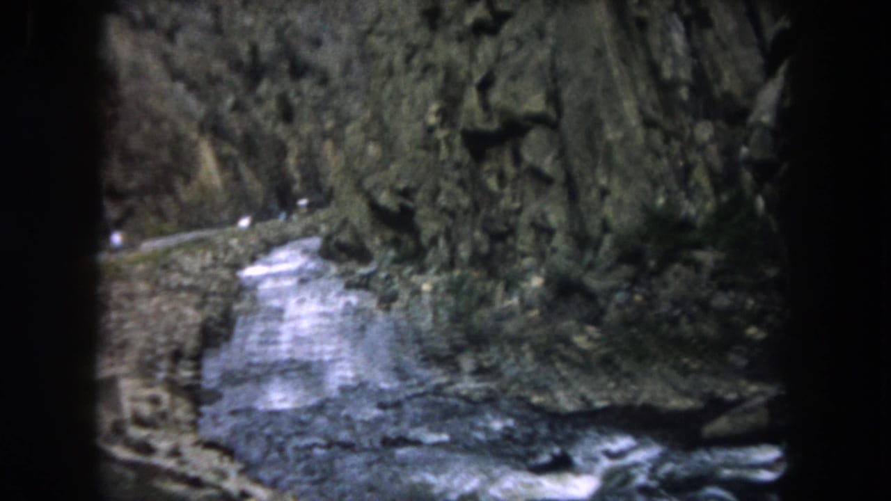 White water bends through a narrow canyon with dark vehicle framing at the edges.