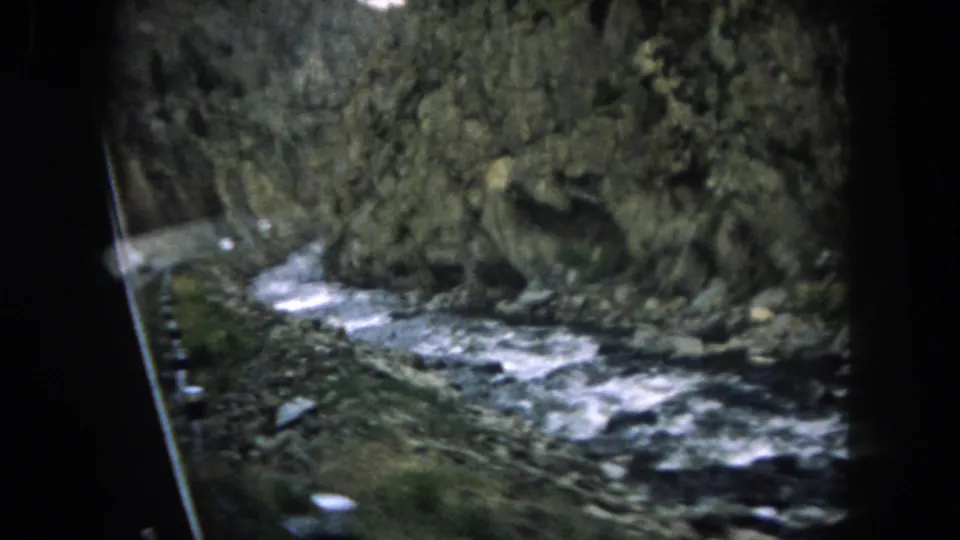 1962 Summit County, Colorado home-movie frame of a fast river below canyon rock, with the vehicle interior crossing the view.