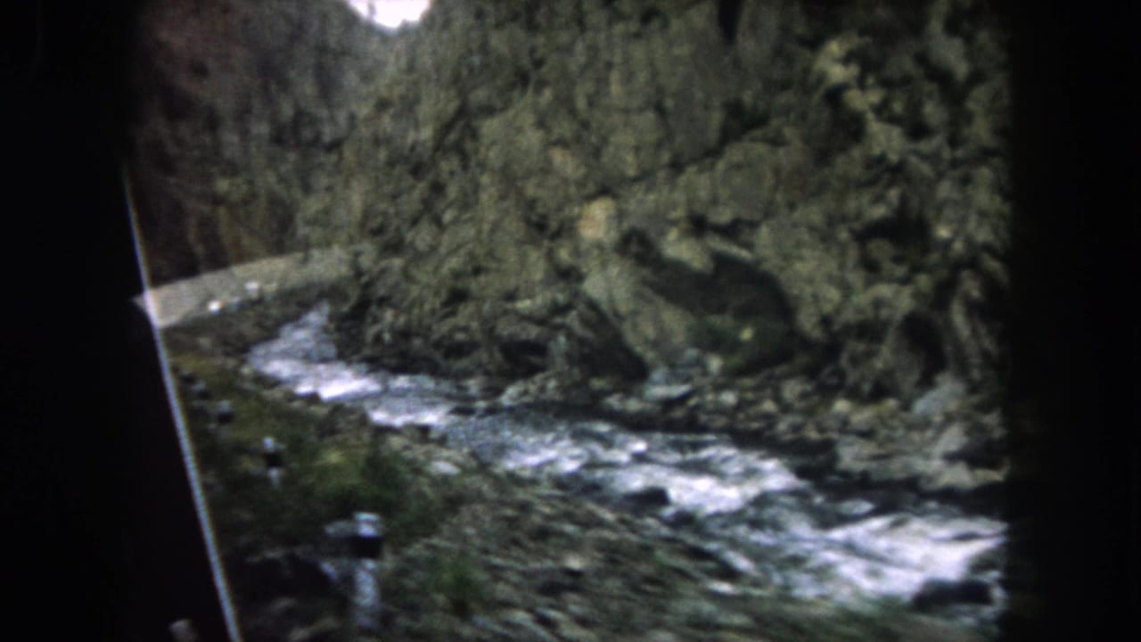 1962 Summit County, Colorado home-movie view of a rushing mountain stream and rugged rock wall from inside a moving vehicle.