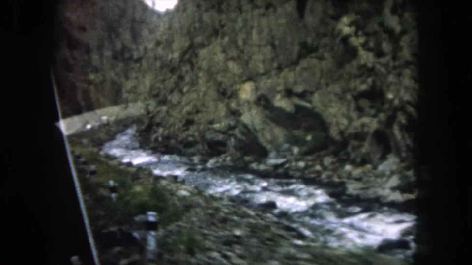 1962 Summit County, Colorado home-movie view of a rushing mountain stream and rugged rock wall from inside a moving vehicle.