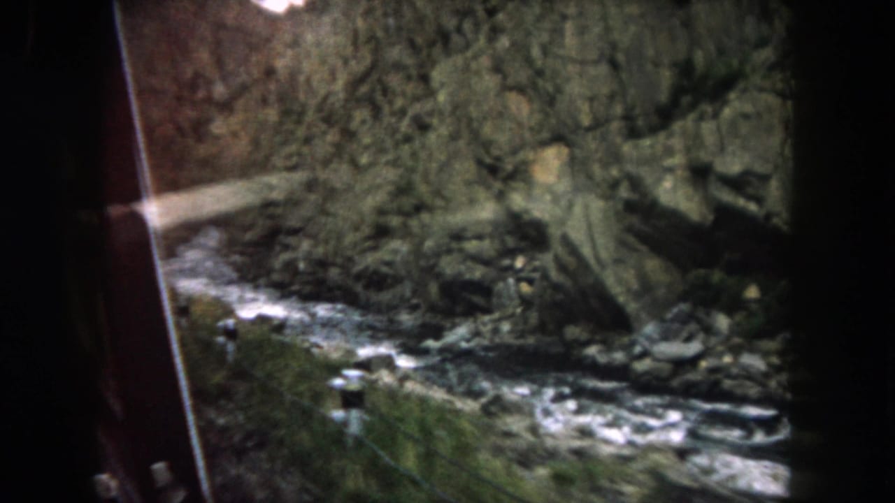 Passenger-window view of a rocky Colorado mountain stream bordered by canyon walls and sparse vegetation.