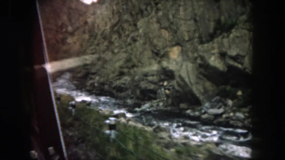 Passenger-window view of a rocky Colorado mountain stream bordered by canyon walls and sparse vegetation.