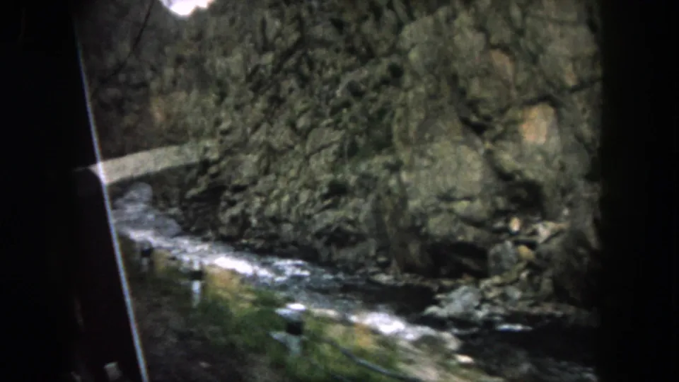 8mm home-movie frame showing a rushing stream below a steep rock face during a 1962 Summit County drive.