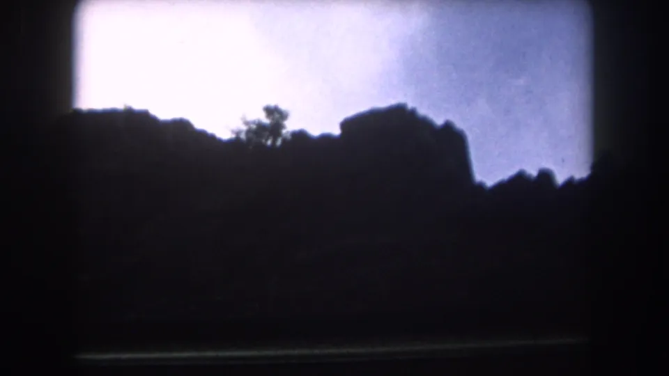 1962 Summit County, Colorado 8mm frame showing a jagged mountain ridge in silhouette below a pale cloudy sky.