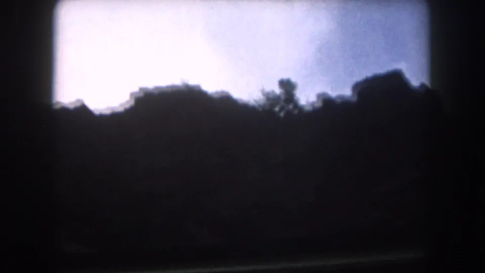 1962 Summit County, Colorado view of a dark ridge line with scattered trees under an overcast sky on 8mm film.