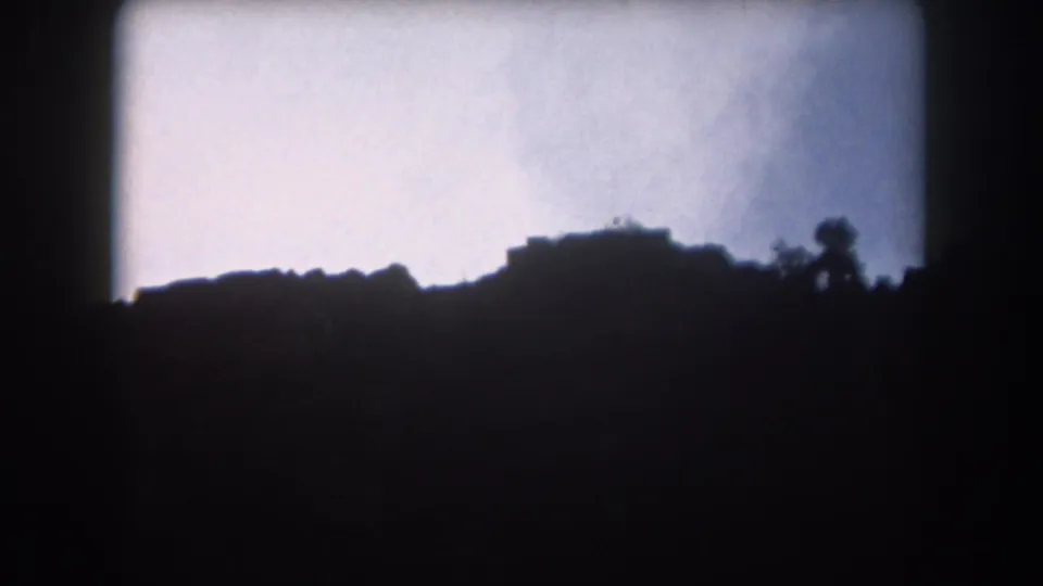 1962 Summit County, Colorado frame with a low silhouetted ridge, a small tree shape, and soft cloudy sky on 8mm film.
