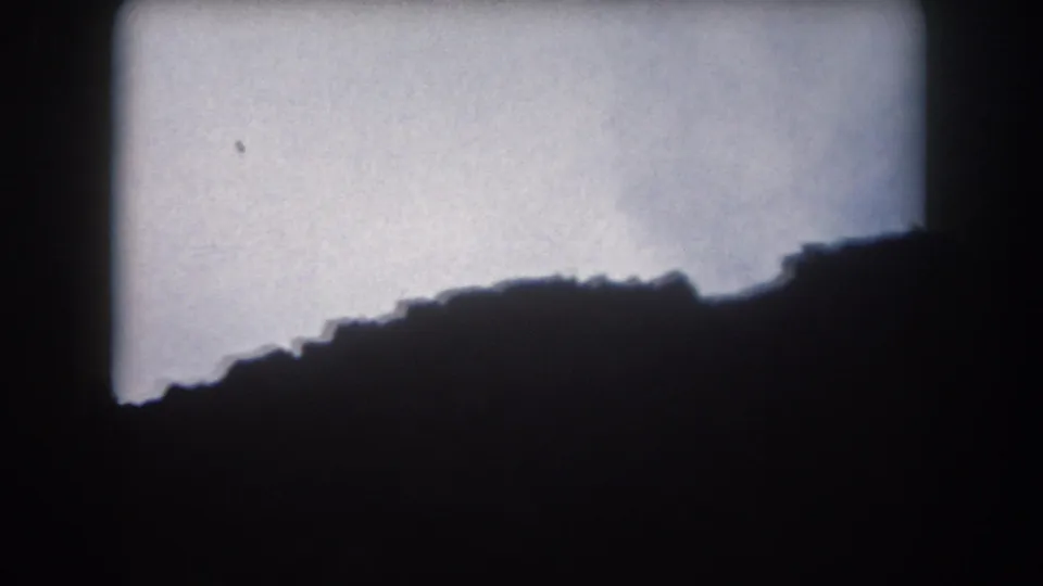 1962 Summit County, Colorado 8mm frame showing a sloping mountain silhouette beneath a bright overcast sky.