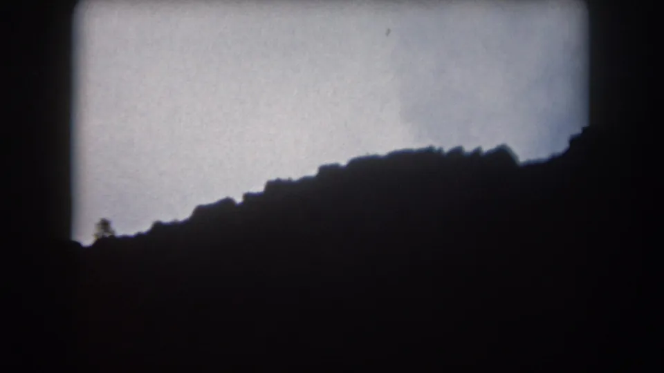 1962 Summit County, Colorado 8mm frame showing a shadowed mountain ridge and faint tree shapes against a pale evening sky.