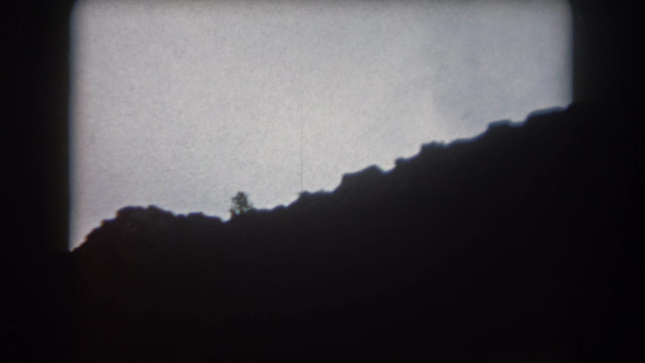 Shadowed ridge rising across the frame with a pale sky and faint tree silhouette.
