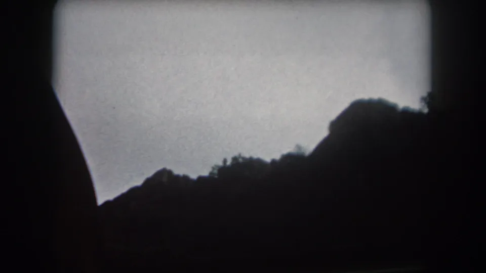 1962 Colorado 8mm frame showing a dark rocky hillside and tree silhouettes beneath a muted dusk sky.