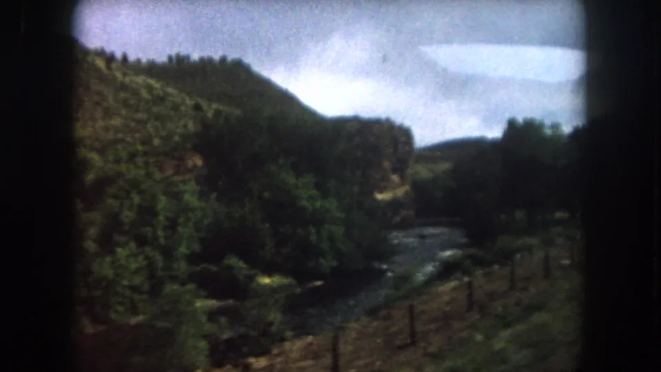 1962 Summit County, Colorado view of a winding river below forested hills, seen from a moving home-movie camera.