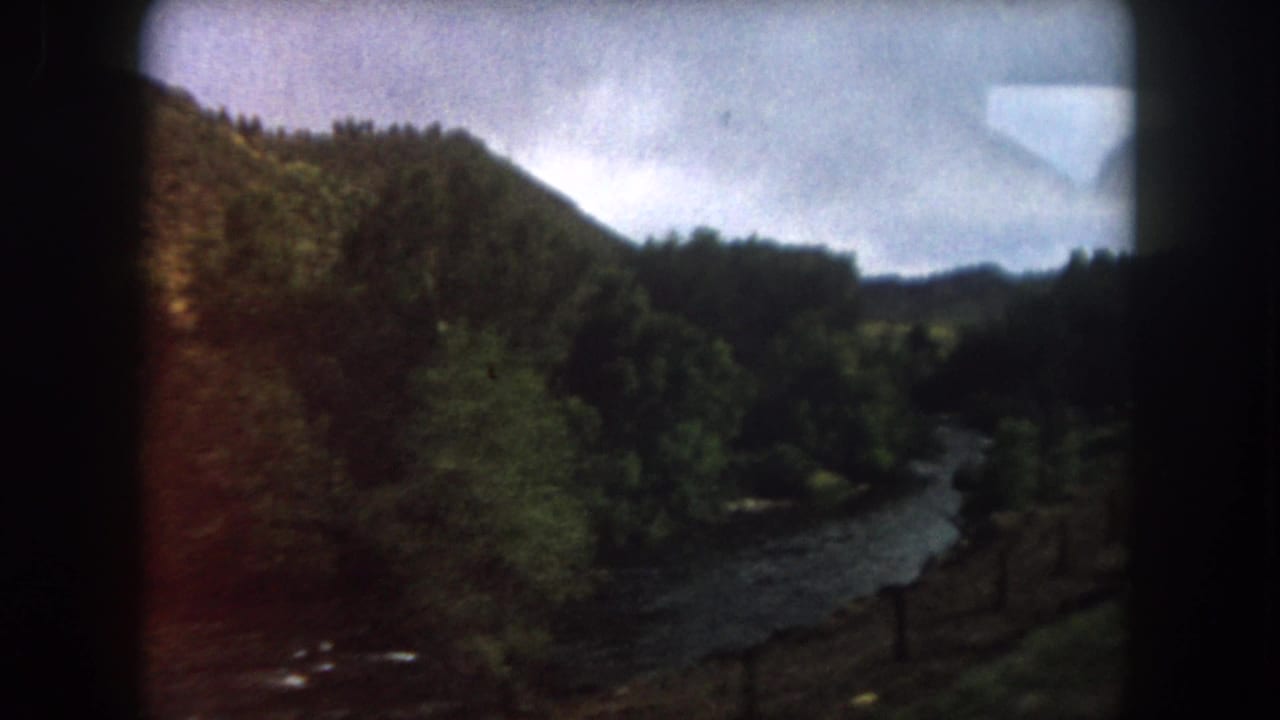 Winding river below wooded hills, framed by dark car-window edges.