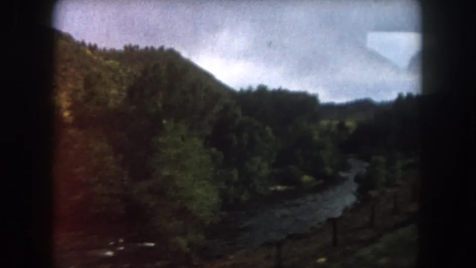 1962 Summit County, Colorado frame with a winding river, tree-covered slopes, roadside fence, and soft 8mm color exposure.