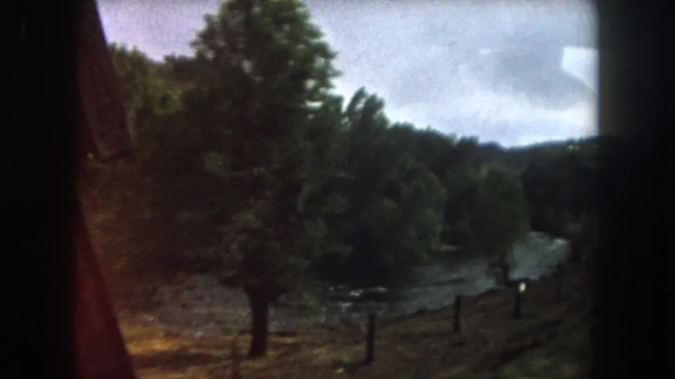 1962 Summit County, Colorado home-movie view of trees, a river bend, fence posts, hills, and dark interior car framing.