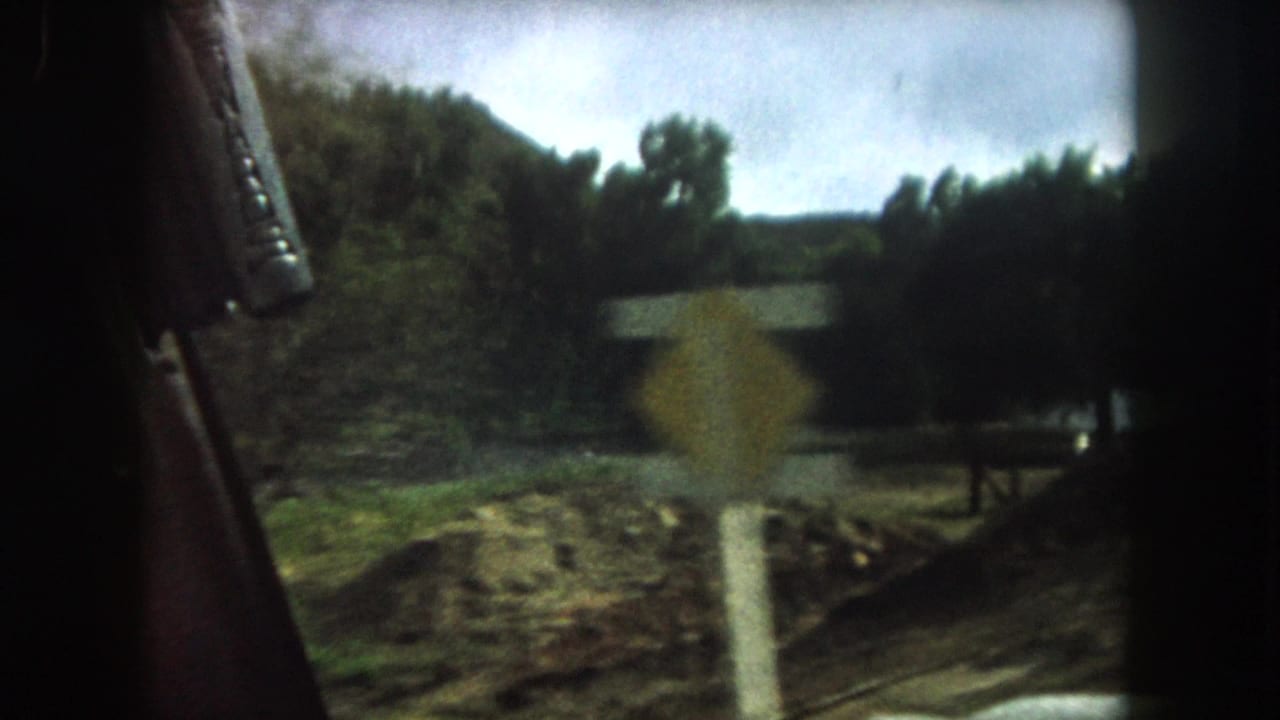 1962 Summit County, Colorado car-window view with a blurred roadside sign, rough ground, trees, and cloudy sky.