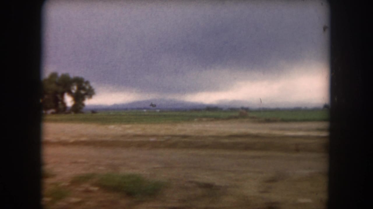 1962 Summit County, Colorado rural field with a small tree cluster, distant low mountains, and a heavy cloudy sky.