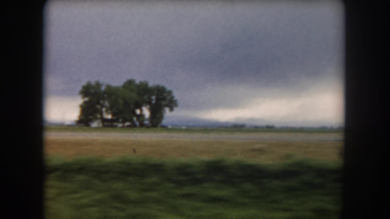 1962 8mm view of cultivated land in Summit County, Colorado, with large trees on the horizon under heavy clouds.