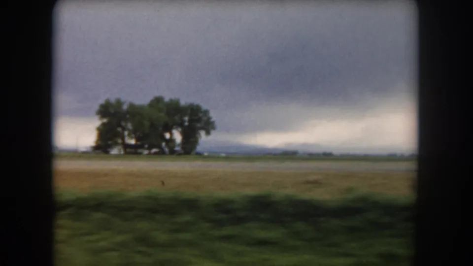 1962 8mm view of cultivated land in Summit County, Colorado, with large trees on the horizon under heavy clouds.