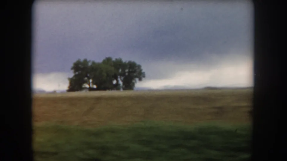Moving 8mm roadside view of Summit County farmland, with a large tree cluster left of center and low clouds across the horizon.