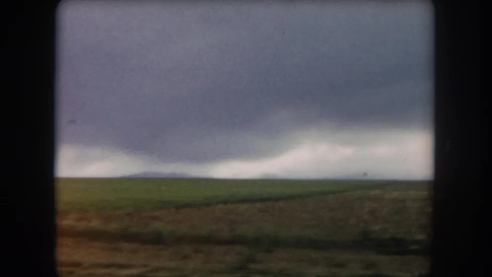 1962 Summit County, Colorado landscape frame with flat green ground, brown field edge, and a dark weather front beyond.