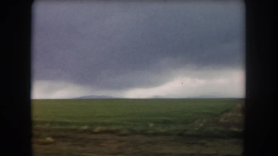 8mm home-movie view of Summit County fields under dark gray clouds, with soft exposure and film grain visible.