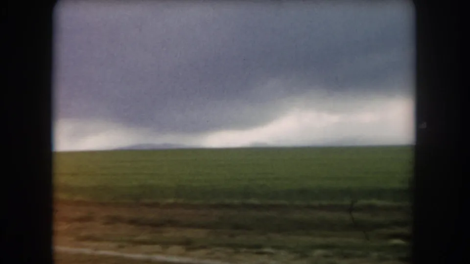 1962 Colorado home-movie view of open green field and brown roadside under a heavy, overcast sky.