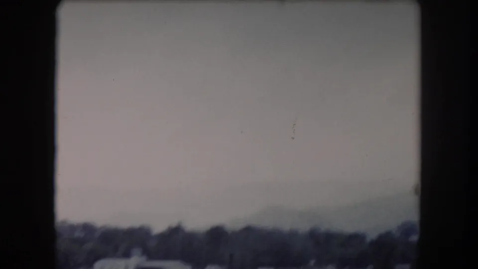 Distant Colorado town edge with trees and low structures under a muted sky, softened by 8mm motion and exposure.